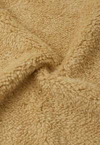 Weiches, flauschiges Material in hellbeige, mit einer strukturierten, plüschigen Oberfläche und einem zerknitterten Aussehen, ideal für Decken oder Überwürfe.