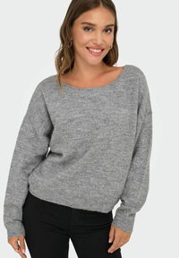Pull gris léger avec un large col bateau et des poignets côtelés. Présente une coupe décontractée et une texture douce, associé à un pantalon noir.