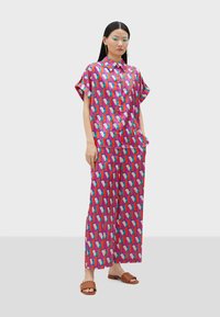 Colorful two-piece outfit featuring a short-sleeve, collared shirt and wide-leg pants, both adorned with a geometric pink, blue, and green pattern.
