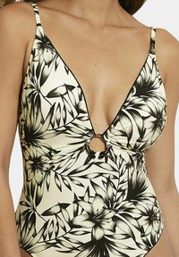 Maillot de bain une pièce floral noir et blanc avec un décolleté en V plongeant, des détails de bretelles et une ouverture frontale circulaire. Tissu texturé.