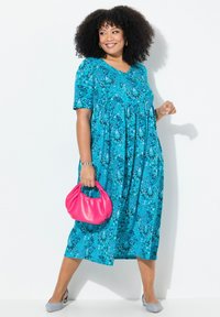 Turkusowa sukienka w kwiaty z krótkimi rękawami, dekoltem w serek i plisowanym pasem. Połączona z różową torebką i jasnoniebieskimi butami.