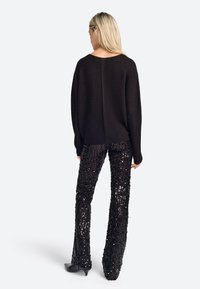 Czarny oversized sweter z okrągłym dekoltem i rozcięciem. Połączony z czarnymi spodniami w dzwony z cekinami, z pionowym wzorem, noszonymi z czarnymi szpilkami.