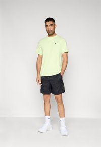 Φωτεινό πράσινο t-shirt της Nike, μαύρο σορτς με σχέδια και λευκά αθλητικά παπούτσια. Το μπλουζάκι έχει ένα μικρό μαύρο λογότυπο στο στήθος.