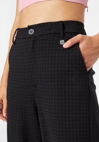 Svart rutiga byxor med ett fint mönster, med knäppning, sidofickor och en mjuk textur.