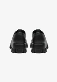 Chaussures en cuir noir avec une semelle épaisse, présentant une semelle extérieure texturée et une languette au talon. Design minimaliste avec une finition lisse.