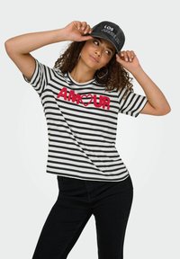 Gestreepte t-shirt in zwart en wit met rode geborduurde tekst "AMOUR". Korte mouwen, ronde halslijn, relaxte fit, gecombineerd met zwarte broek.