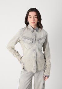Camicia in denim grigio chiaro con colletto a punta, due tasche sul petto e dettagli di cucitura sottili. Presenta una vestibilità comoda e maniche lunghe.