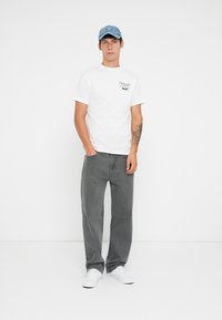 Camiseta blanca de manga corta con texto impreso, combinada con jeans rectos grises y zapatillas blancas, rematada con una suave gorra azul.