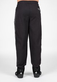 Zwarte broek met wafelstructuur en een taps toelopend ontwerp, voorzien van zijstrepen en een relaxte tailleband. GeCombineerd met zwarte hoge sneakers.