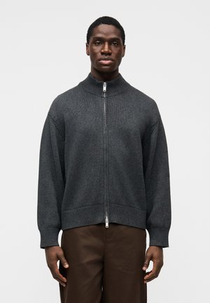 Tumši pelēka džemperis ar rāvējslēdzēju, ar ribotu apkakli un aprocēm, pilna priekšpuses rāvējslēdzēja un brīva piegriezuma dizains.