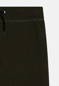 Pantalons de survêtement verts foncés avec une taille côtelée, un cordon noir, et des détails de couture visibles. Fabriqués en matériau doux et texturé.