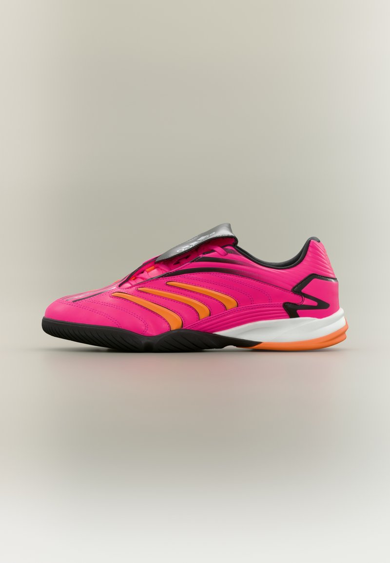 Φωτεινό ροζ παπούτσι για εσωτερικό ποδόσφαιρο με πορτοκαλί ρίγες, μαύρη σόλα και ασημένιο κάλυμμα κορδονιών σε ουδέτερο φόντο.