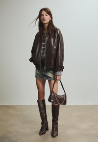 Smeđa kožna bomber jakna, sivi prugasti pulover, traper mini suknja, čizme do koljena s teksturiranim uzorkom i mala torbica s zakovicama.