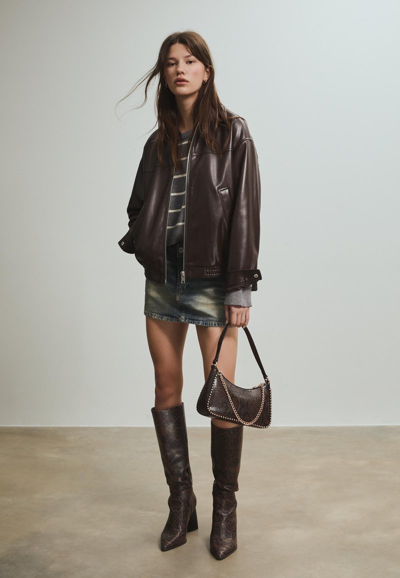 Smeđa kožna bomber jakna, sivi prugasti pulover, traper mini suknja, čizme do koljena s teksturiranim uzorkom i mala torbica s zakovicama.