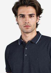 Marine poloshirt van een gestructureerde stof, met een drie-knopenpolo en een contrasterende kraag met witte en blauwe strepen. Klein logo op de borst.