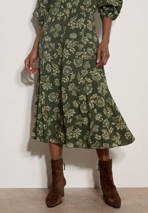Grüner Midirock mit floralem Muster, kombiniert mit braunen Wildleder-Stiefeletten, teilweise Ansicht von der Taille bis zu den Füßen.