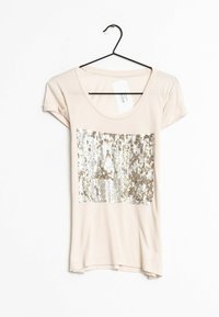 Světle béžové tričko s kulatým výstřihem a krátkými rukávy, se stříbrným a zlatým flitrovým vzorem přes oblast hrudníku.