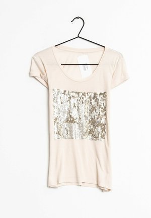 Ljust beige t-shirt med rund halsringning och korta ärmar, pryds av en paljett-design i silver och guld över bröstområdet.