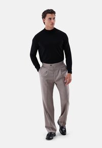 Schwarzes Langarmshirt, graue, plissierte Hose und schwarze Schuhe. Glatter Stoff, maßgeschneiderte Passform und dezente Muster auf der Hose.