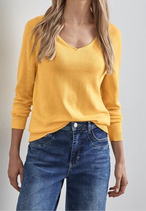 Gul V-hals sweater med lange ærmer, ribbede manchetter, парret с tætsiddende blå denim jeans med traditionelle syninger og fem-lomme design.