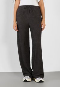 Pantalons larges gris foncé avec une texture côtelée, dotés d'une taille élastique et d'un cordon de serrage. Associés à des baskets blanches et violettes.