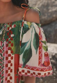 Vestido off-the-shoulder en tejido ligero que presenta un vibrante estampado botánico con acentos en rojo, verde y rosa. Detalle de dobladillo en forma de ondas.