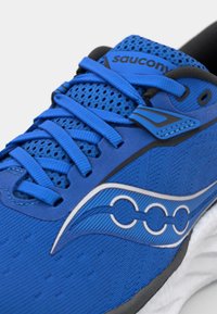 Scarpa da corsa blu con tomaia in rete testurizzata, lacci piatti e sovrapposizioni sintetiche. Presenta un design a onde bianche e una suola ammortizzata.