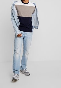 Lässiges Outfit mit einem farblich blockierten Pullover in Weiß, Grau und Marineblau, kombiniert mit hellblauen Jeans und grauen Sneakern.