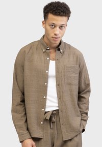 Brown textured button-up shirt with long sleeves, chest pocket, and white buttons, worn over a white tank top.