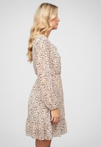 Robe courte de couleur blush avec un ourlet à volants, ornée d'un délicat motif floral et dotée de manches longues, fabriquée en tissu léger et transparent.