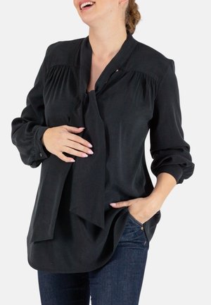 Zwarte blouse met strik hals, voorzien van plooien op de schouders en lange mouwen, gemaakt van lichtgewicht, gladde stof. Draag met blauwe jeans.