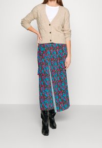 Beige knitted cardigan with v-neck and three buttons. Floral-patterned maxi skirt in teal, pink, and purple with a side slit. Black knee-high boots.