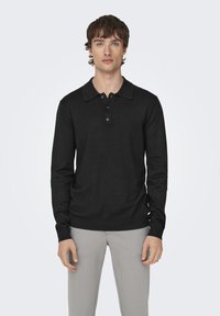 Schwarzes Langarm-Polohemd mit klassischem Kragen und Knopfleiste mit drei Knöpfen. Der Stoff wirkt weich und hat eine leicht taillierte Form.