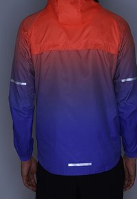 Chaqueta ligera con un diseño degradado que va del rojo al morado. Incluye detalles reflectantes en los hombros y el dobladillo inferior.