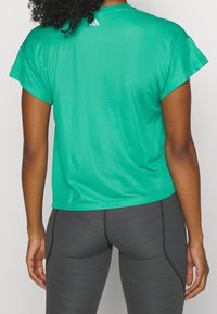 Grön mesh idrottströja med korta ärmar, med rund halsringning och en liten logotyp på den övre ryggen. Matchad med grå åtsittande leggings.