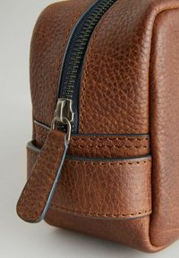 Borsa in pelle marrone con superficie texturizzata, dotata di una cerniera scura e di un tirante. Decorata con cuciture intorno alla base.