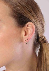 Gouden oorbellen met een kleine bolvormige stud en een geometrische V-vormige accentuering. Het ontwerp benadrukt een strak, minimalistisch stijl.