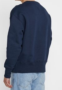 Marineblauwe sweatshirt met ronde hals, verlaagde schouders en ribbels aan de mouwen en onderkant. Zacht materiaal met minimale stikdetails op de achterkant.