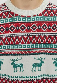 Rode gebreide trui met feestelijke patronen, waaronder groene rendieren, geometrische ontwerpen en een geribbelde witte ronde hals. 