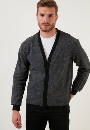 Cárdigan gris oscuro con un escote en V de canalé negro, botones frontales y mangas largas. Textura suave, con un ribete contrastante a lo largo de los bordes.