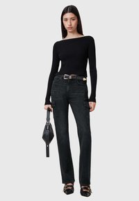 Top negro de manga larga con textura de canalé combinado con jeans negros estilo cargo y zapatos de punta negra. Los accesorios incluyen un pequeño bolso negro.