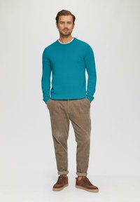 Tyrkysový sveter s dlhými rukávmi, okrúhlym výstrihom; khaki kordové nohavice; hnedé tenisky s akcentmi; jednofarebné pozadie.