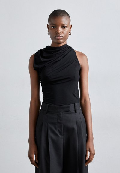 Haut noir sans manches avec un tissu drapé et un décolleté asymétrique, associé à un pantalon noir plissé taille haute. Texture lisse.