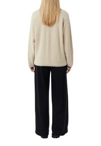 Beżowy, puszysty sweter z długimi rękawami, noszony z luźnymi czarnymi spodniami. Sweter ma miękką fakturę i luźny fason.