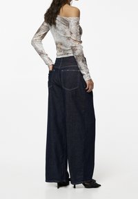 Weite, dunkelblaue Jeans mit hoher Taille und Gesäßtaschen, kombiniert mit einem figurbetonten, schulterfreien silbernen Oberteil mit strukturiertem Muster.