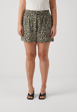 Vrouw draagt losse beige en zwarte korte broek met elastische taille, witte top en zwarte open teen sandalen met hak, staand op witte vloer.