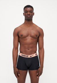Crne bokserice s laganom rozom Nike logotip trakom. Tkanina se čini glatkom i rastezljivom, s uskim fitom. Jednostavan dizajn, bez uzoraka.