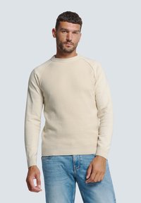 Crème kleurige gebreide trui met een ronde hals, ribbeltextuur en raglan mouwen, gecombineerd met lichtblauwe spijkerbroek. Soepel, casual ontwerp.