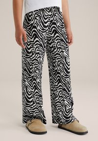 Črne in bele hlače s potiskom zebra, širokega kroja, izdelane iz teksturirane tkanine, v kombinaciji s bež natikači.