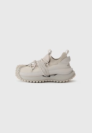 Light gray sneakers with a textured sole, elastic straps, and a cushioned ankle. Designed with a rounded toe and minimalistic silhouette.